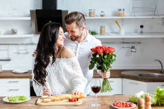 幸福的夫妇做饭，而男人拿着玫瑰花束