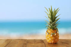 在海滩和热带背景前的木桌上，菠萝