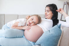 年轻的孕妇和她的小女儿在室内。孩子和她妈妈在等一个小宝宝。幸福的家庭期待.