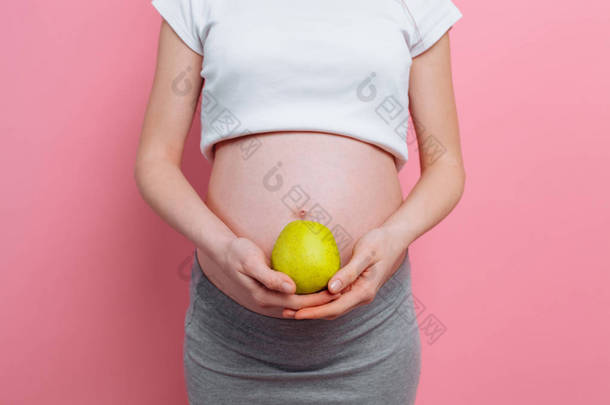 Pregnant woman holding a green apple near the belly. The concept of pregnancy, motherhood, proper nu