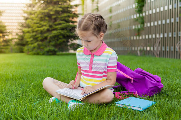 开学的第一天。女学生小学生坐在学校附近的草地上，画着笔记本。观念回到学校。户外活动