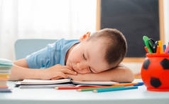 小学生坐在教室里躺着书桌，书桌里塞满了书，培训教材，小学生懒洋洋地睡着，无聊极了