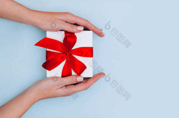 女性的手与指甲保持礼品盒与红丝带淡蓝色背景。 节日的概念.
