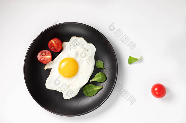 煎鸡蛋，在黑盘上煎鸡蛋，加上新鲜的生菜和西红柿。在白色背景上隔离.