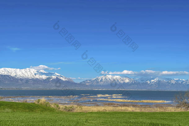 阳光明媚的蓝天下，有湖面和雪山景色的草地