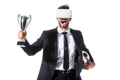 兴奋的商人在虚拟现实耳机与足球和奖杯杯隔离在白色