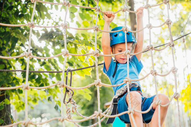 夏天阳光明媚,可爱的小男孩在攀岩探险公园里享受活动。攀岩极限运动与头盔和保险