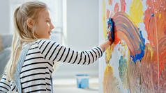 快乐的小女孩,双手浸在生动的油漆画在墙上五颜六色的抽象。她有乐趣和笑。家正在装修.