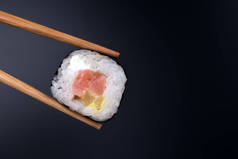 Sushi roll with chopsticks close up on black background