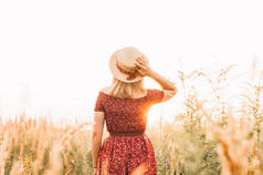美丽的女孩在红色礼服在黄色走过田野，日落时间。黄金时间。乡村风光