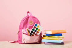 粉红色背包与用品在口袋里附近的彩色书籍隔离在粉红色