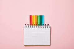 彩色毡笔的顶视图，靠近空白笔记本，在粉红色上隔离