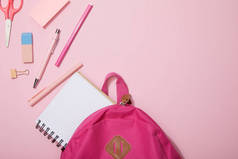 分散的学校用品和空白笔记本附近的背包隔离在粉红色的顶部视图