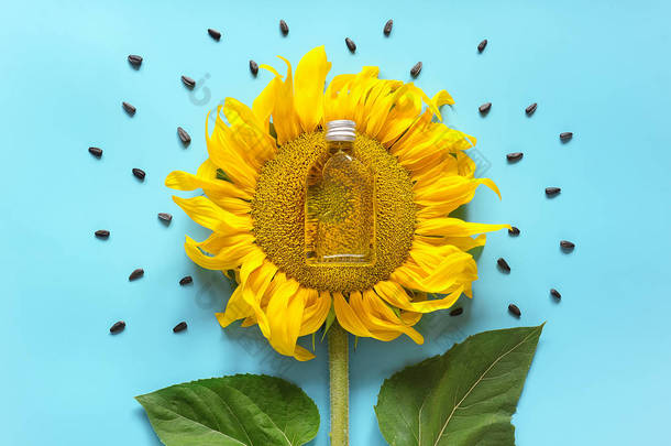 瓶天然葵花籽油，种子和新鲜的黄色向日葵在蓝色背景。创意概念有机植物油生产，收获时间。顶视图， 平铺， 模板