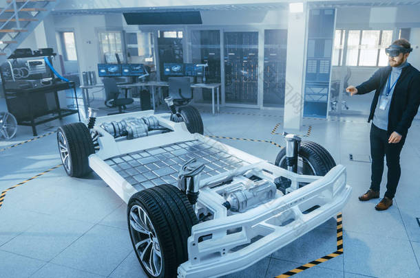 汽车工程师在电动车底盘平台上工作，使用增强现实耳机。在创新实验室设施概念车架包括车轮，悬架，发动机和电池.