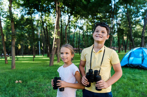 <strong>happy</strong> kids smiling while holding binoculars near camp