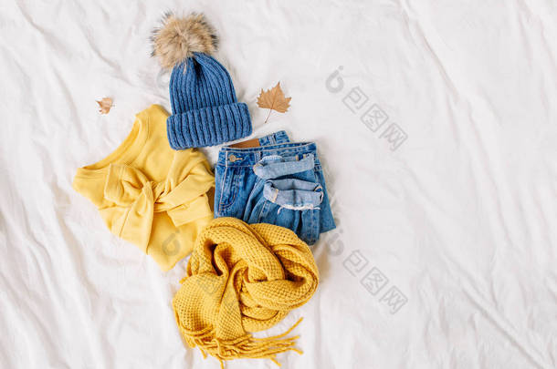 舒适的黄色毛衣，蓝色牛仔裤，围巾和帽子在床上的白床单。女士时<strong>尚</strong>的<strong>秋冬</strong>套装。时髦的服装拼贴画。平铺，顶视图.
