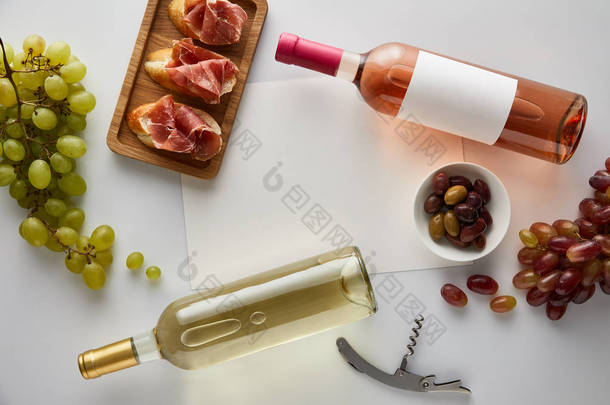 葡萄酒、软木塞、空<strong>白纸</strong>、橄榄和切碎的意大利煎饼、白底面包等附近的白葡萄酒和玫瑰酒的顶部视图