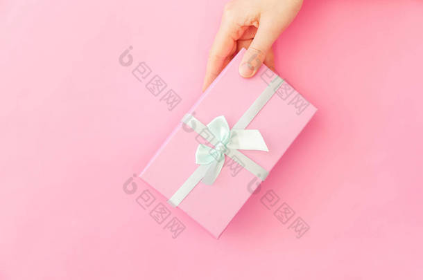 简单的设计女性手拿着粉红色的礼品盒隔离在粉红色柔和的色彩时尚背景