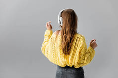 穿着黄色毛衣跳舞的女孩在用灰色耳机听音乐时的倒影