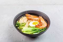 亚洲面汤、虾仁拉面、蔬菜和鸡蛋在灰色混凝土背景的黑色碗中。 平躺在地上,俯瞰,模拟,头顶. 健康食品概念