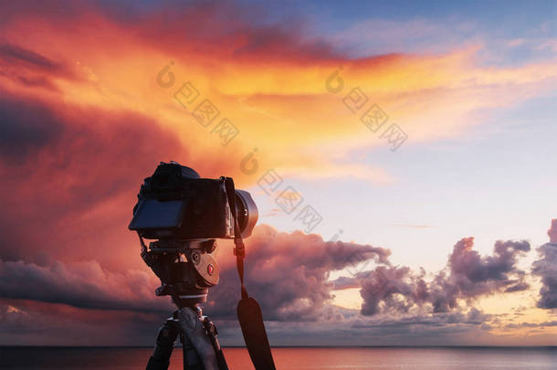 夕阳西下的大海，海滨。 西边的火球,在地平线上,在五彩斑斓的橙色天空中. 神奇的积雨云 <strong>前进方向</strong>三脚架上的Dslr相机