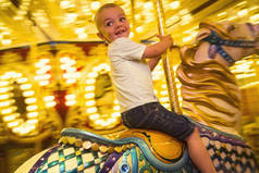 可爱的小男孩在游乐园或嘉年华骑旋转木马很开心。快乐的小男孩骑着欢乐的小旋转木马，带着明亮的灯光