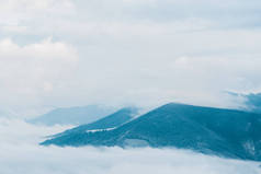 白色蓬松的云彩覆盖着松树的雪山风景