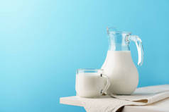 玻璃瓶和杯子，牛奶放在蓝色背景的白色木制边缘.
