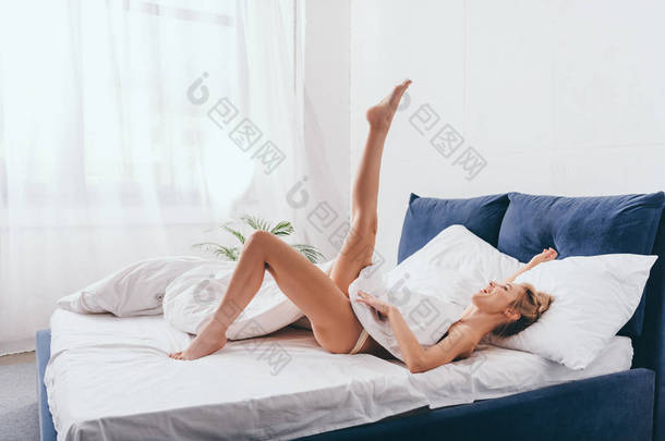 早上，一个快乐而有趣的女人躺在床上，两条腿平躺在床上