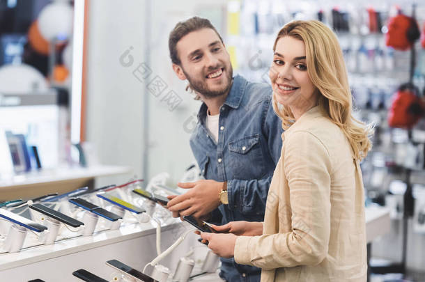 微笑的男女朋友在家用电器商店里拿着新的智能手机