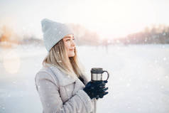 美丽快乐的女人户外的冬天。喝热茶或降雪咖啡的笑女孩