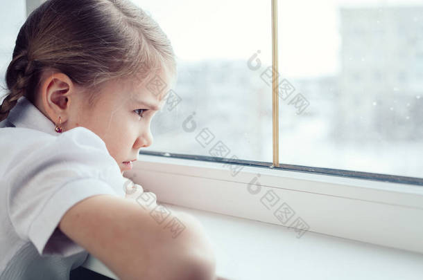 一个悲伤的小女孩在白天坐在窗边。悲伤的概念.