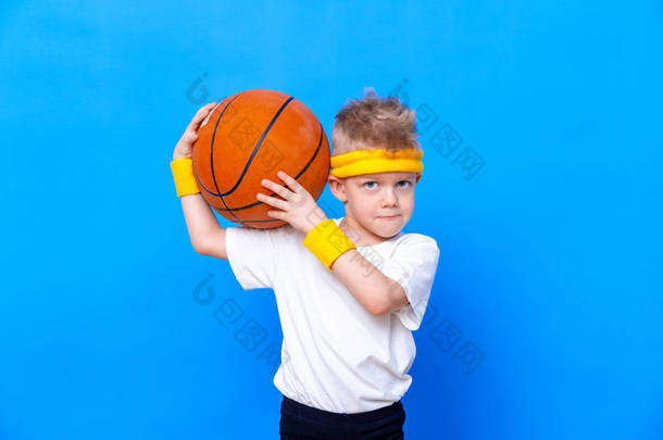 一个身材矮小的小男孩,背负着蓝色工作室背景的篮球运动.体操运动。儿童运动员。活动。体育。健康、健康和精力。成功