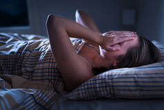 失眠，睡眠呼吸暂停或压力的概念。半夜不眠的女人醒着，蒙着脸。女士无法入睡。梦魇或沮丧。头痛或偏头痛的痛苦.