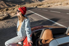 Woman traveling by the red car on a desert road