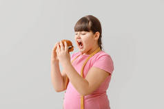 体重超标的女孩，有浅色背景的不健康汉堡包