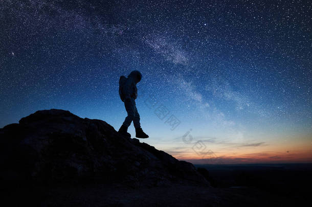 宇航员在美丽的夜空下与星星一起下山。宇航员穿着太空服探索新星球的轮廓。宇宙中的空间旅行、星系和人类的概念