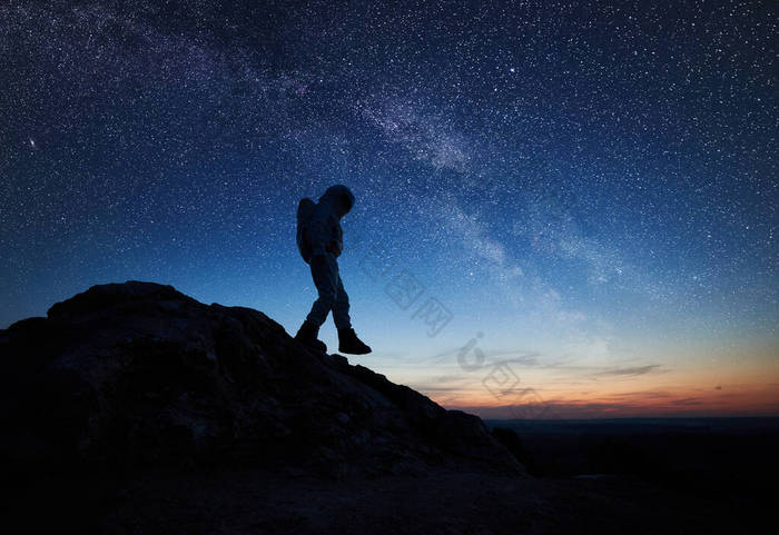 宇航员在美丽的夜空下与星星一起下山。宇航员穿着太空服探索新星球的轮廓。宇宙中的空间旅行、星系和人类的概念