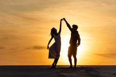 日落时分，男人和女人在海滩上迎着太阳跳舞的轮廓