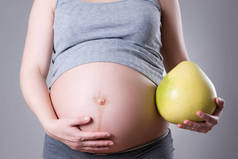 怀孕与营养- -身披石榴灰色背景的孕妇，摄影棚拍摄