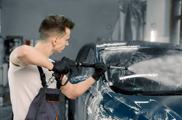 一个工人在洗车时用高压水清洗现代蓝色汽车的侧角视图。洗车服务及详细概念