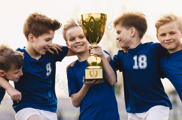 孩子们赢得了足球赛。一群快乐的男孩拿着金杯.学校运动队庆祝胜利.足球运动队的孩子们高兴极了