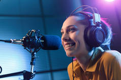 年轻、面带微笑的女人，戴着耳机，对着收音机的话筒说话，娱乐和交流的概念