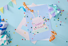 蓝色背景的礼品盒和生日贺卡附近彩色彩斑斓的五彩纸屑的顶部视图