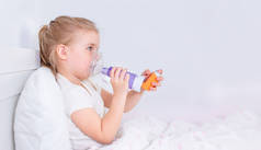 生病的小女孩躺在床上躺着吃哮喘药。有卧床吸入器治疗咳嗽的病童。流感季节。为年轻病人提供的卧室或医院房间。保健和药物治疗