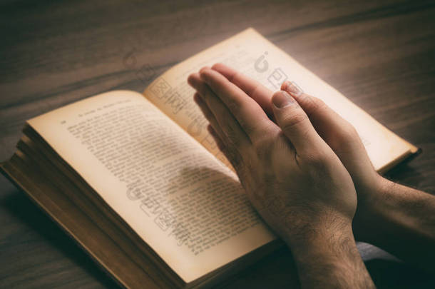 祈祷，男人交出一本打开的书神圣的圣经，木制的书桌背景。<strong>信仰</strong>、宗教和精神<strong>信仰</strong>概念