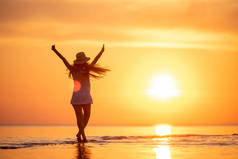 年轻快乐的女孩在夕阳西下的海滩举起双臂