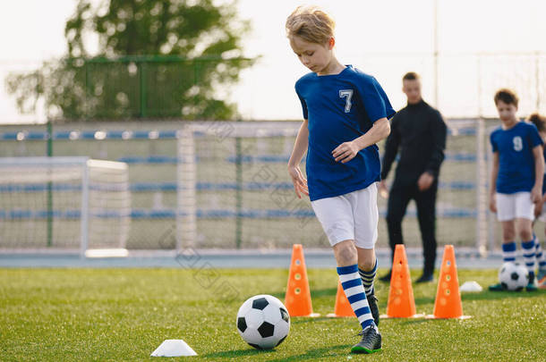 足球训练:冰雹训练.青少年足球练习赛。年轻的足球运动员在球场上训练.足球飞镖锥形钻。穿着红色足球球衣的男孩穿着球衣在球杆间跑动