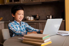 在隔离期间，带着笔记本电脑和书籍在网上学习的亚洲男孩微笑着